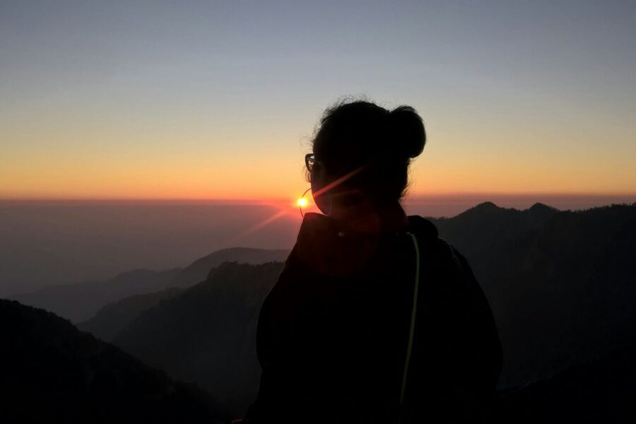 a woman standing on top of a mountain at sunset